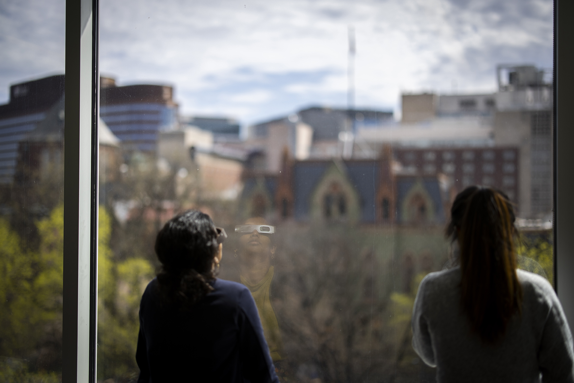 Two people watch the eclipse out of a window looking toward College Hall on Penn’s campus.