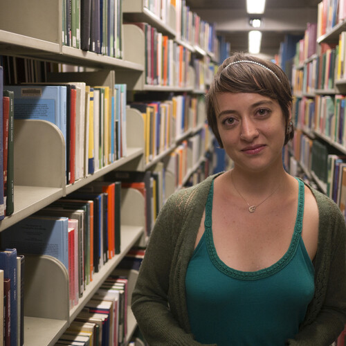 A person standing in a library stack, with shelves of books on either side.