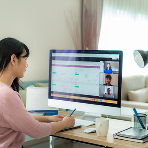 a person sits at a desktop computer at home watching a work video conference