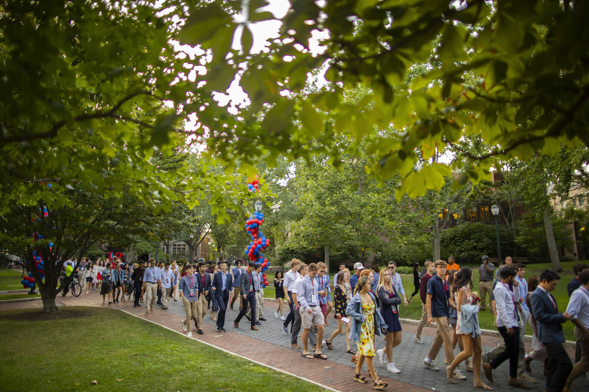 Class of 2023 walks down Locust Walk at dusk towards convocation on College Green.