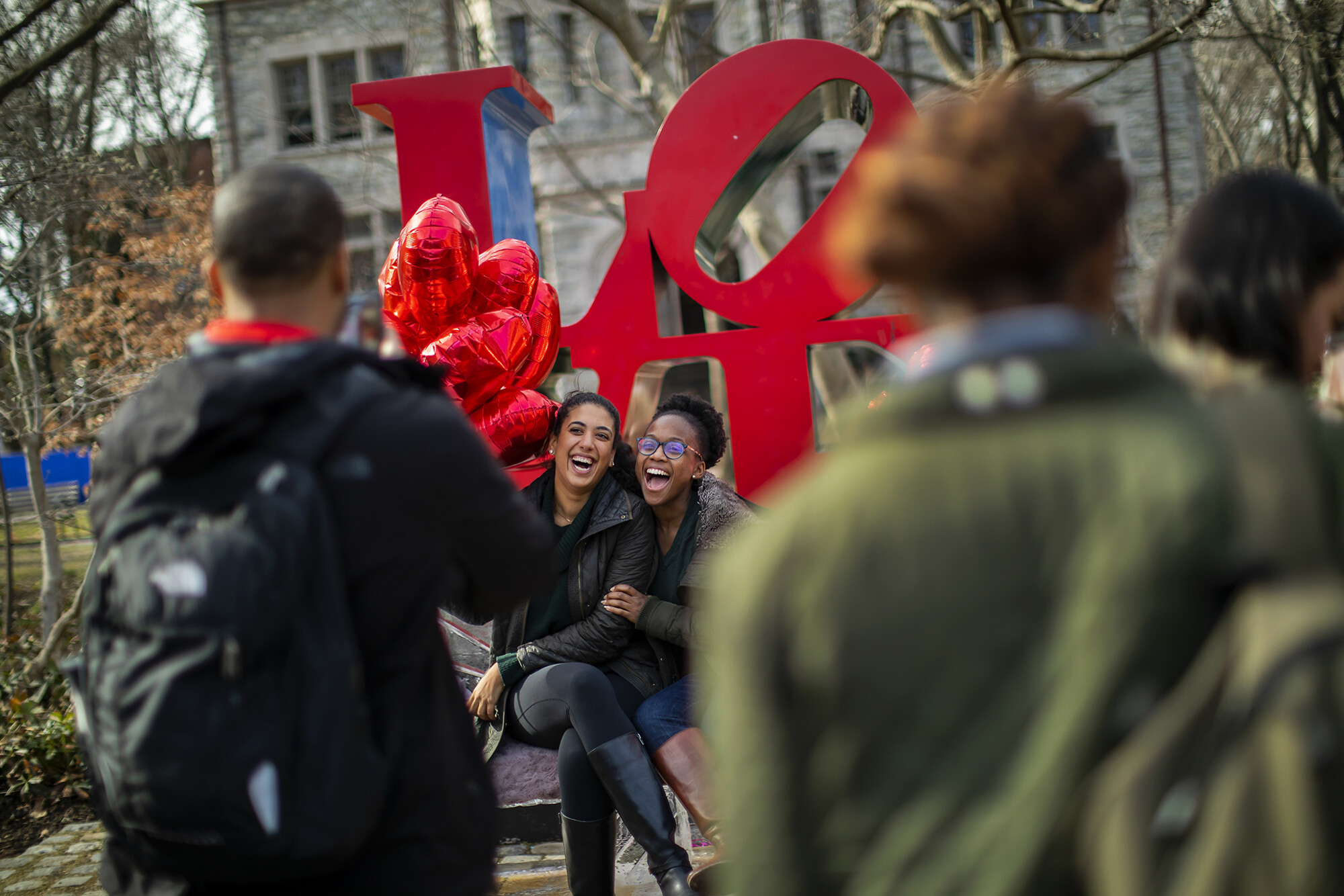 students with heart balloons sitting on Robert Indiana’s LOVE statue on Penn’s campus.