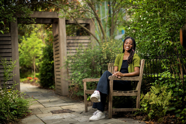 Deborah Olatunji sits on a bench in springtime outside the Kelly Writers House