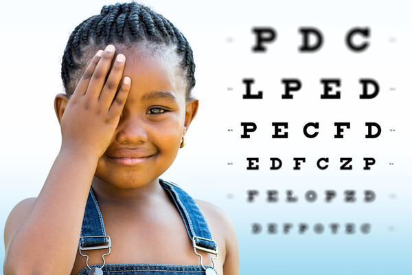 young child covering one eye with a hand with eye chart letters on the right side