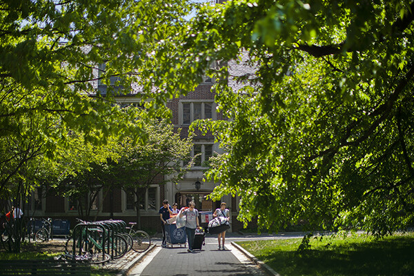 Students with carts and bags walking down a walkway on campus in the daylight during Move-Out.