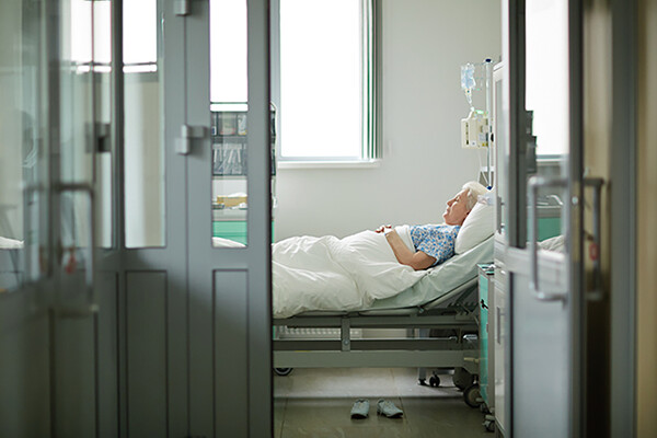 edlerly patient lying in hospital bed with door open and sunlight coming through the windows.