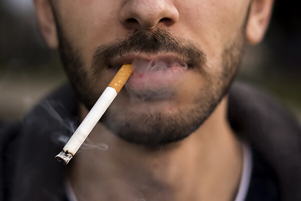 Closeup of bottom third of a young person's face smoking a cigarette