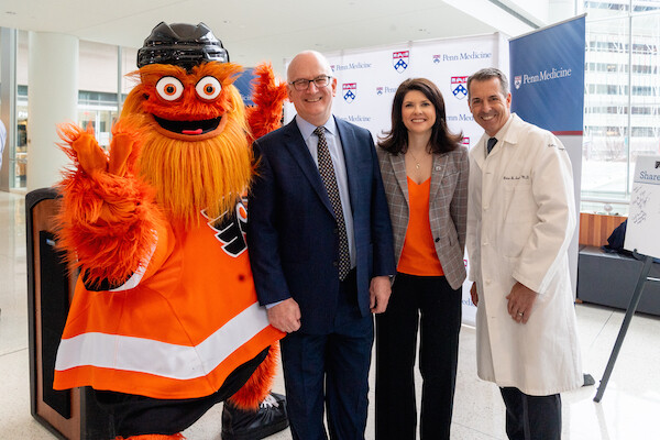 Philly Flyers’ mascot Gritty waves while standing beside Kevin Mahoney, Valerie Camillo, President of Business Operations for the Philadelphia Flyers & Wells Fargo Center and Penn Medicine’s Brian Sennett.