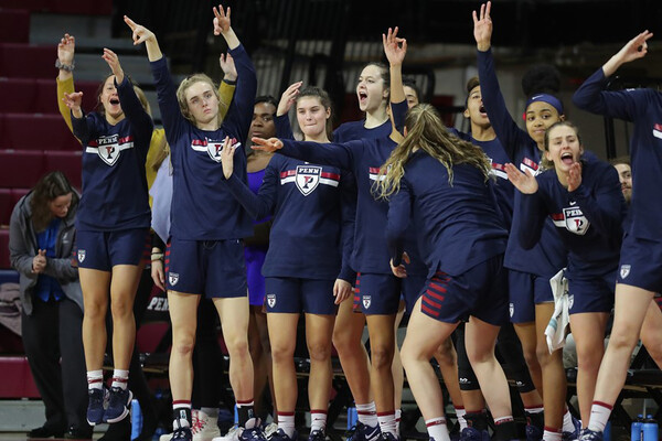 After a teammate hits a three-pointer, women's basketball players on the bench celebrate and hold up three fingers.