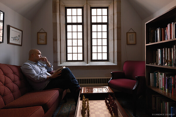 University minister sitting on a sofa in his office by a window.