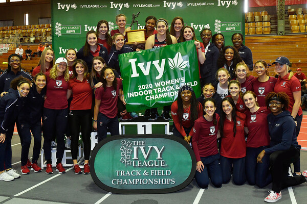 Athletes on the women's track and field team pose with a championship banner after winning the Indoor Ivy Heps.