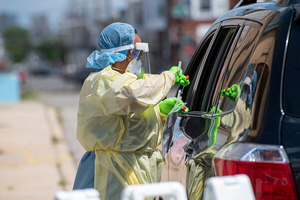 A health care worker in personal protective gear swabs a person in a vehicle at a drive-up COVID testing site.