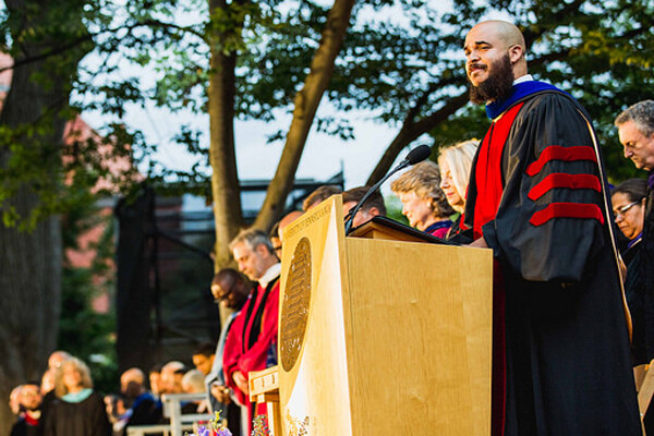Charles Howard stands at a podium in a commencement robe during Commencement