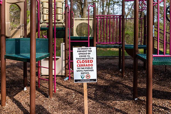 Sign mounted at a playground that reads “In order to prevent the spread of COVID-19, this facility is closed (cerrado) to the public until further notice.”