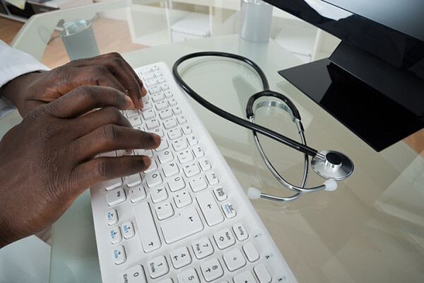 doctor typing on computer keyboard with stethoscope on desk