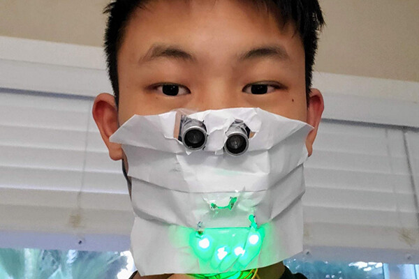 Face of high school student wrapped in a paper face covering mask with sensors attached that are glowing green.