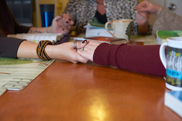 Three people with hands clasped sit around a dining table