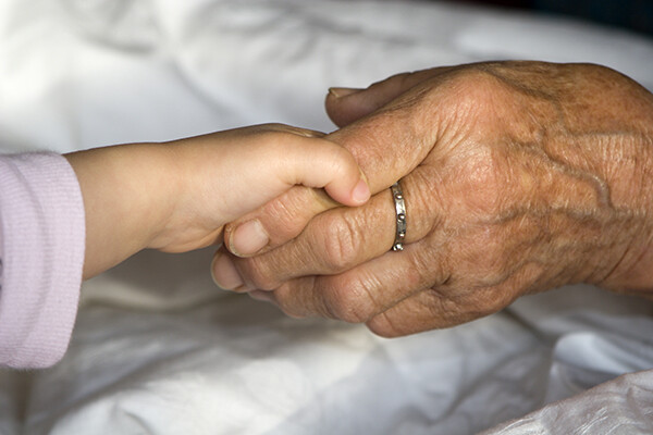 A small child’s hand holding the pointer finger of an elderly person’s hand.