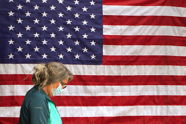 Person wearing a face mask walking past a large American flag.