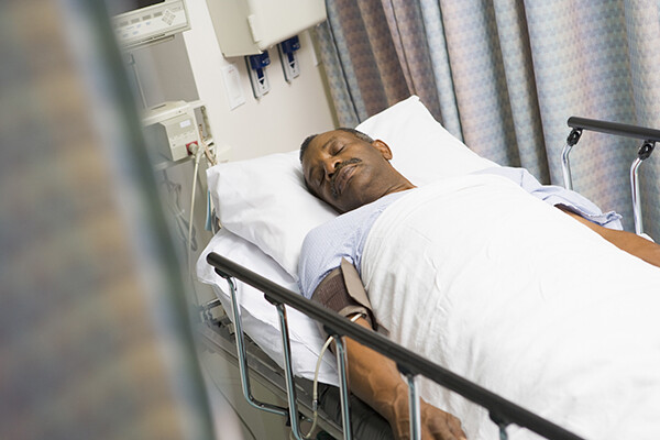 African American person lying on a hospital bed asleep.