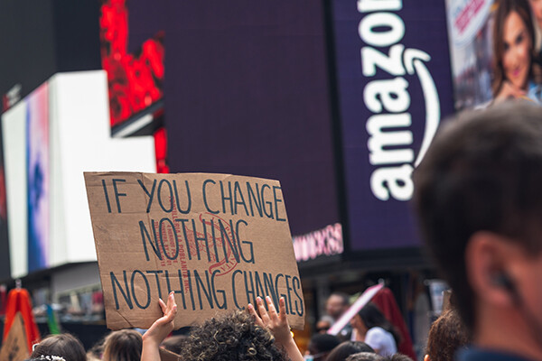 Person in demonstration crowd holding a sign that reads IF YOU CHANGE NOTHING NOTHING CHANGES.