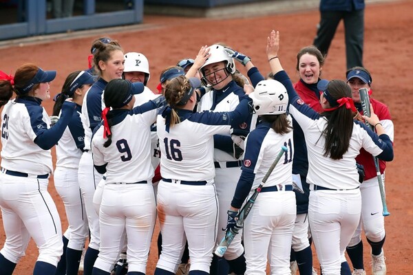 Members of the women's softball congratulate a player at home plate, patting her on the head.