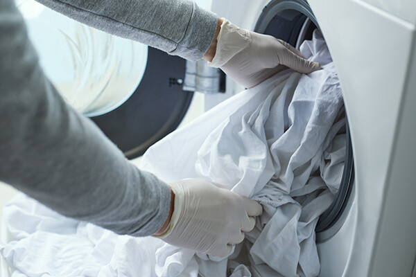 Person wearing latex gloves pulling bed sheets out of a dryer.