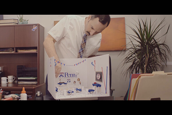 Film still from Eat Wheaties! showing Tony Hale building a Penn-themed diorama on a desktop.