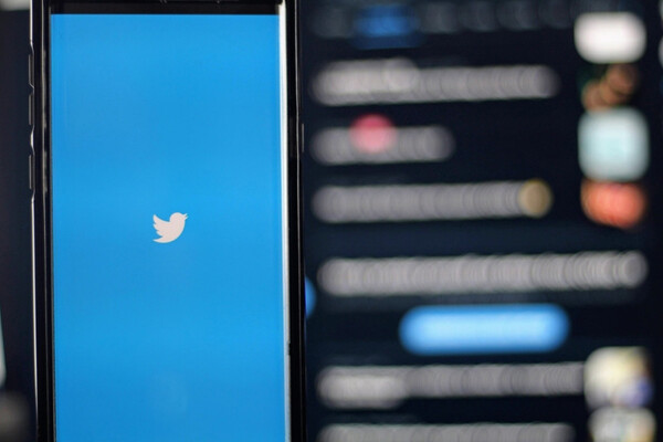 Smart phone with Twitter logo in front of a blurry computer screen in the background.