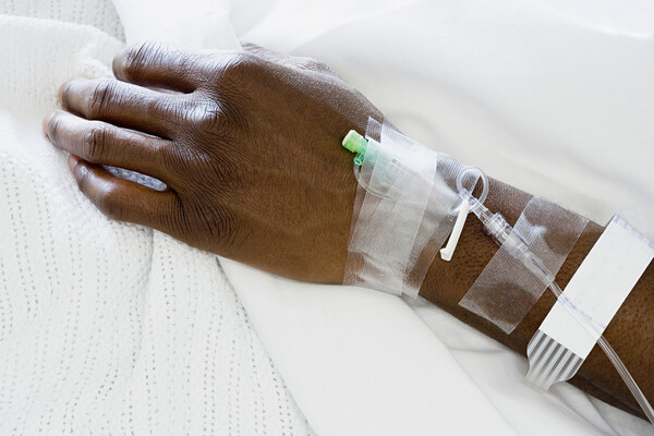 Hand of an African American person on a hospital bed with a hospital bracelet and an IV drip.
