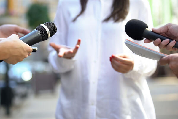 Two hands holding microphones questioning a person talking.