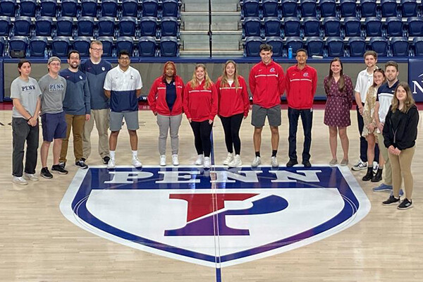 Penn Athletics interns stand at center court at the Palestra near the Penn logo