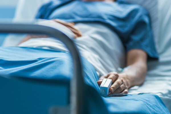 Image of a person laying in a hospital bed, with a pulse oximeter on their finger.