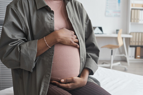 Pregnant person holding their belly in a doctor’s office.