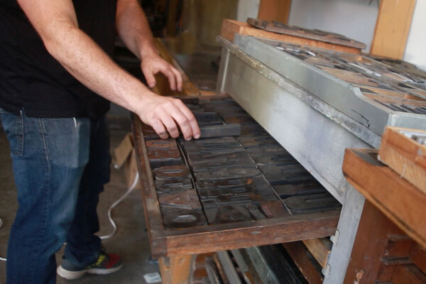 Person holding a printing type at an old-fashioned printing press.