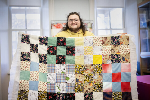 Luke Godsey holds a multicolored quilt up at the PWC