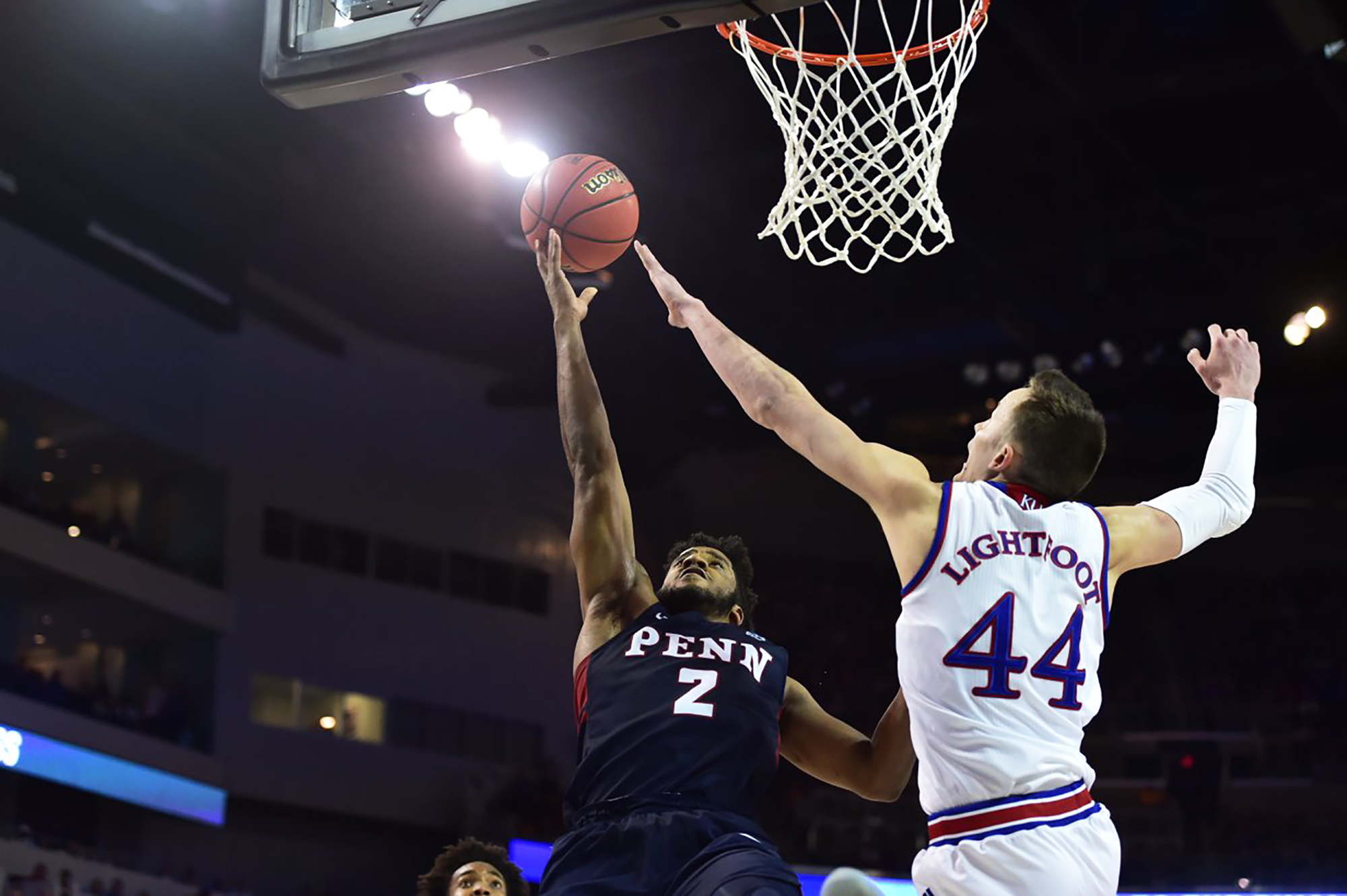 Two basketball players reach for the ball under the hoop