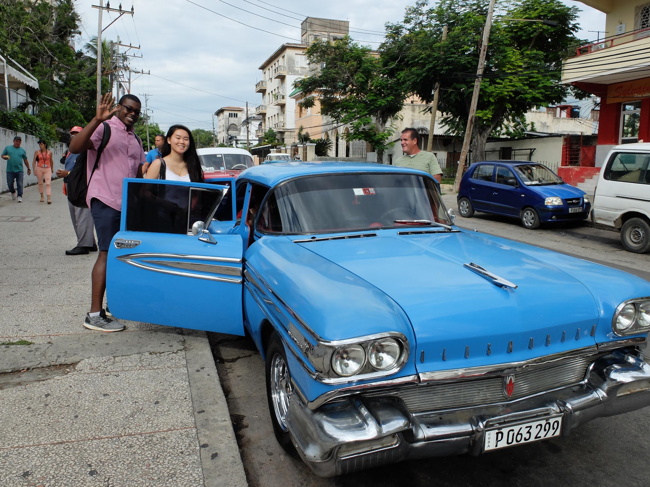 Two-Penn-students-standing-by-classic-bright-blue-Oldsmobile-car-in-Cuba.
