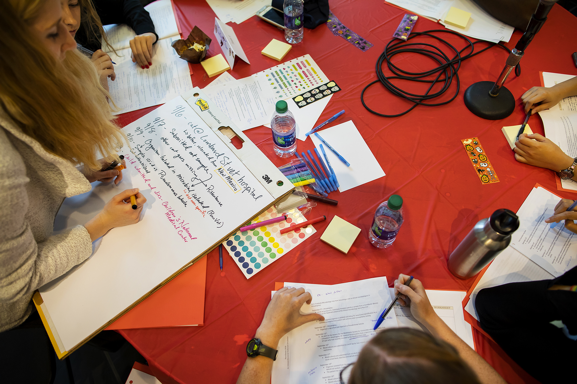 Students work at a table covered with paper, water bottles and markers