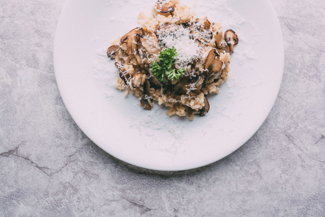 Mushroom risotto on a white plate garnished with white cheese shreds and parsley