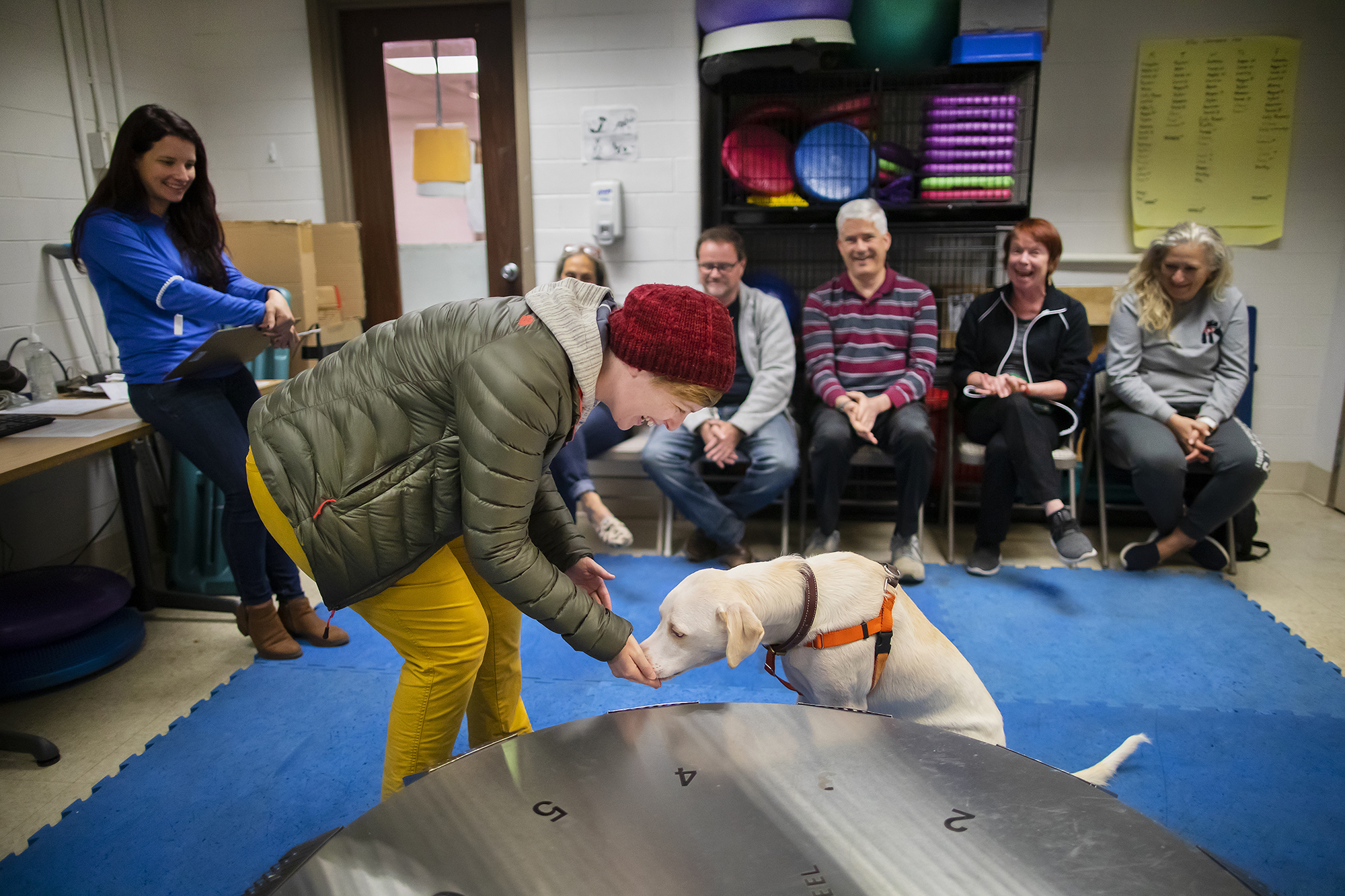 Melissa Hopkins leans over to give a treat to her dog Cedar as instructor Meghan Ramos and other class participants look on
