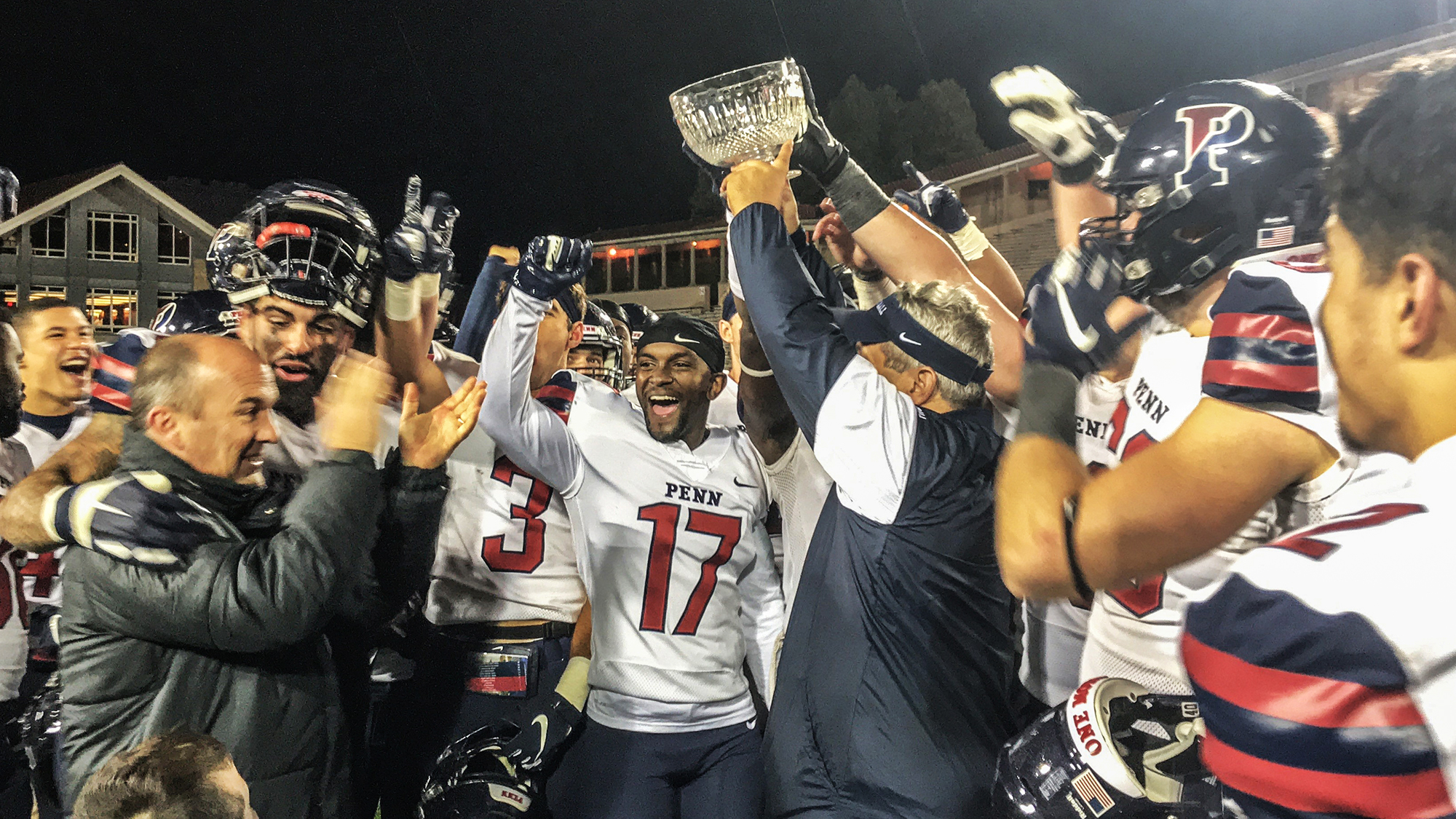 Penn football players hold up trophy after beating Cornell
