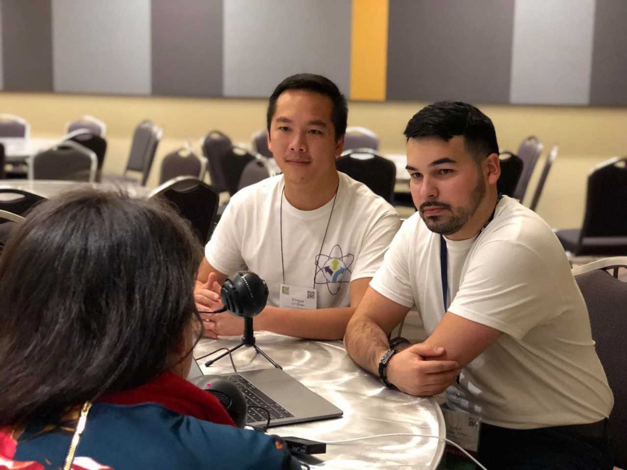 With a microphone between them, Enrique Lin-Shiao and Kevin Alicea-Torres sit for an interview with one of the subjects of their podcast. 