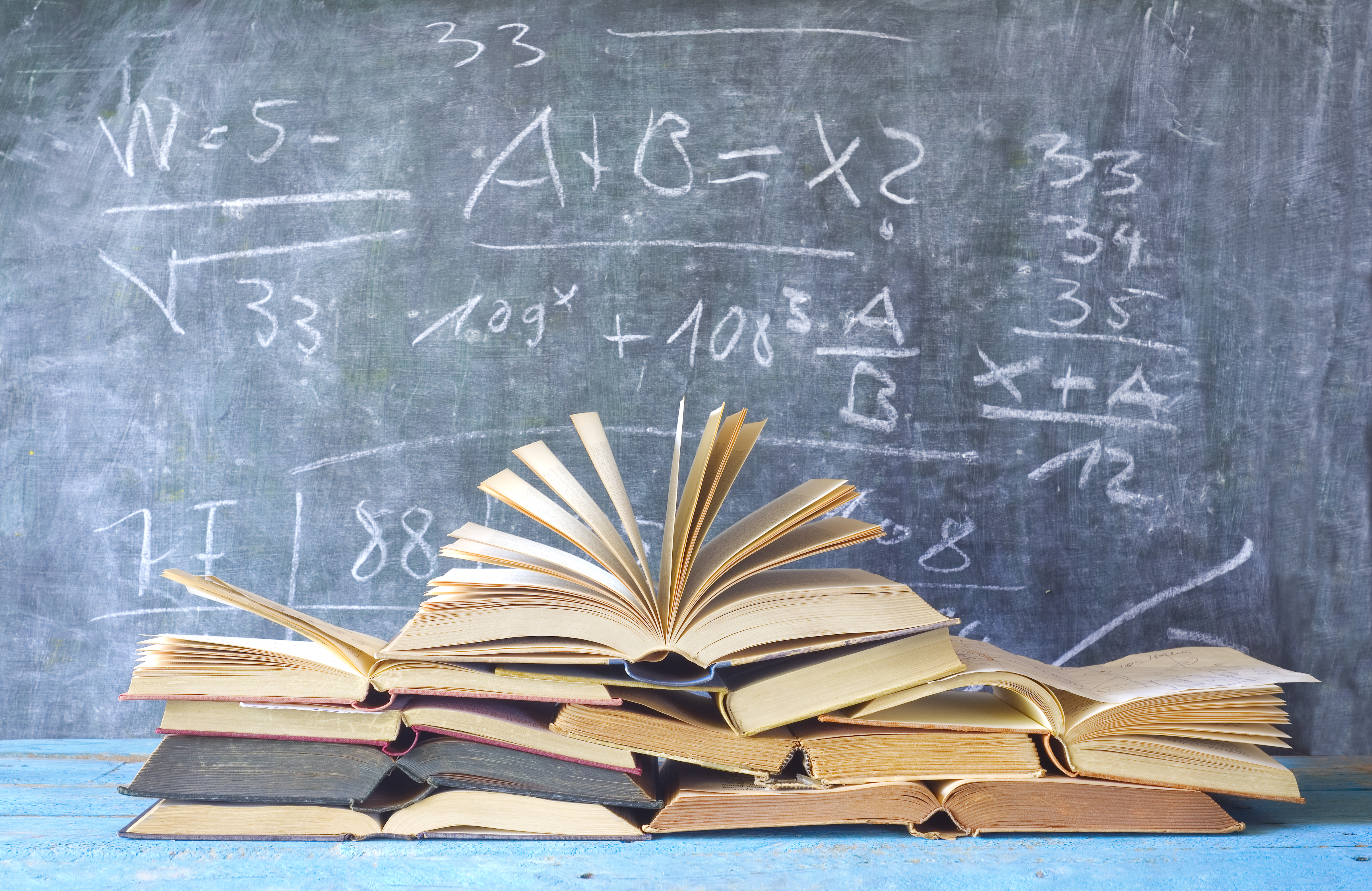 a stack of books in front of a chalkboard with math equations