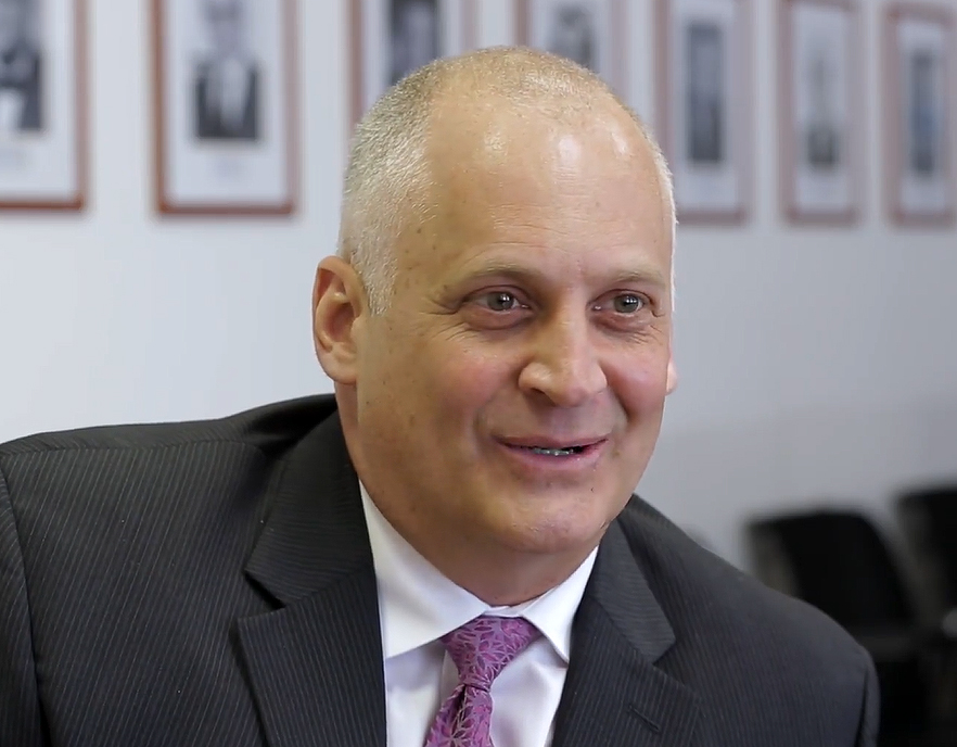 Smiling man in a grey suit with a purple tie.