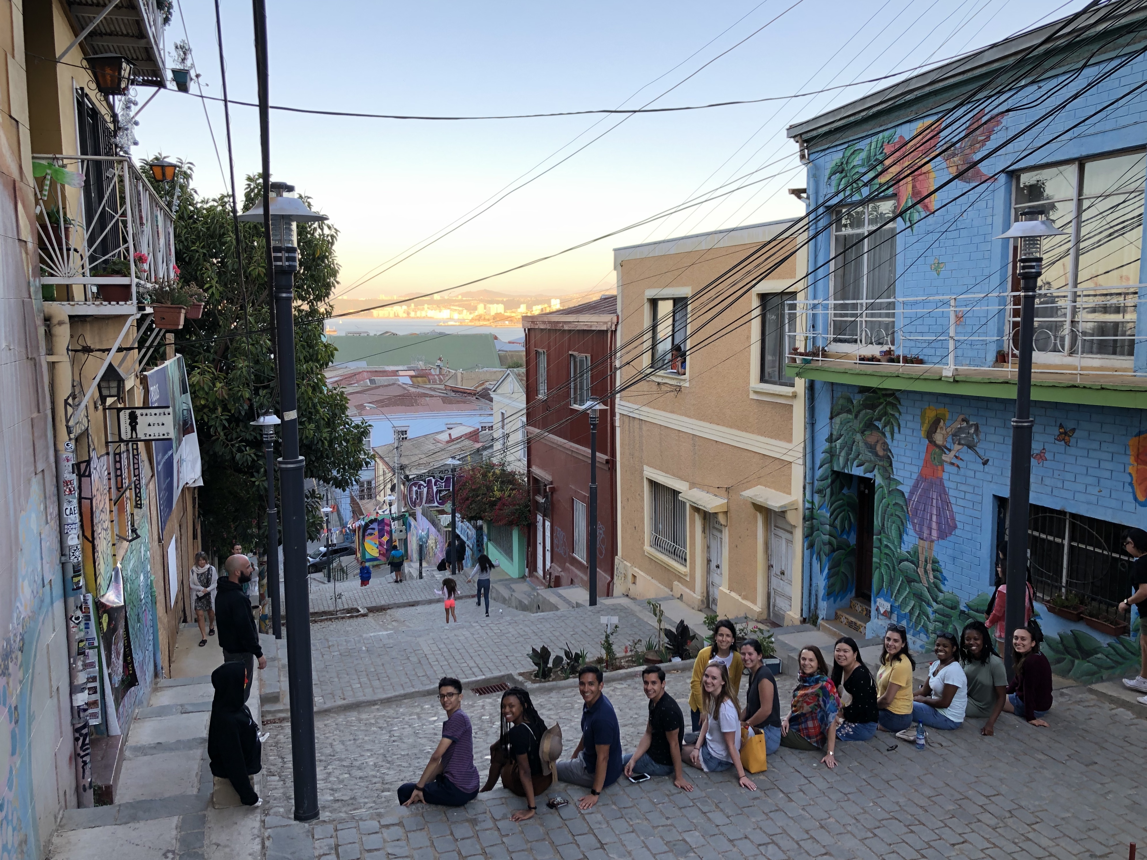 A group of college students sitting on a street between colorful buildings.