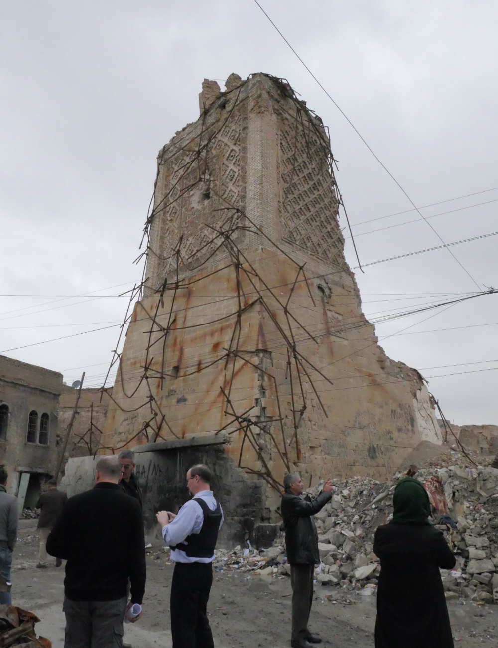 A brown brick minaret destroyed with people in the foreground. 