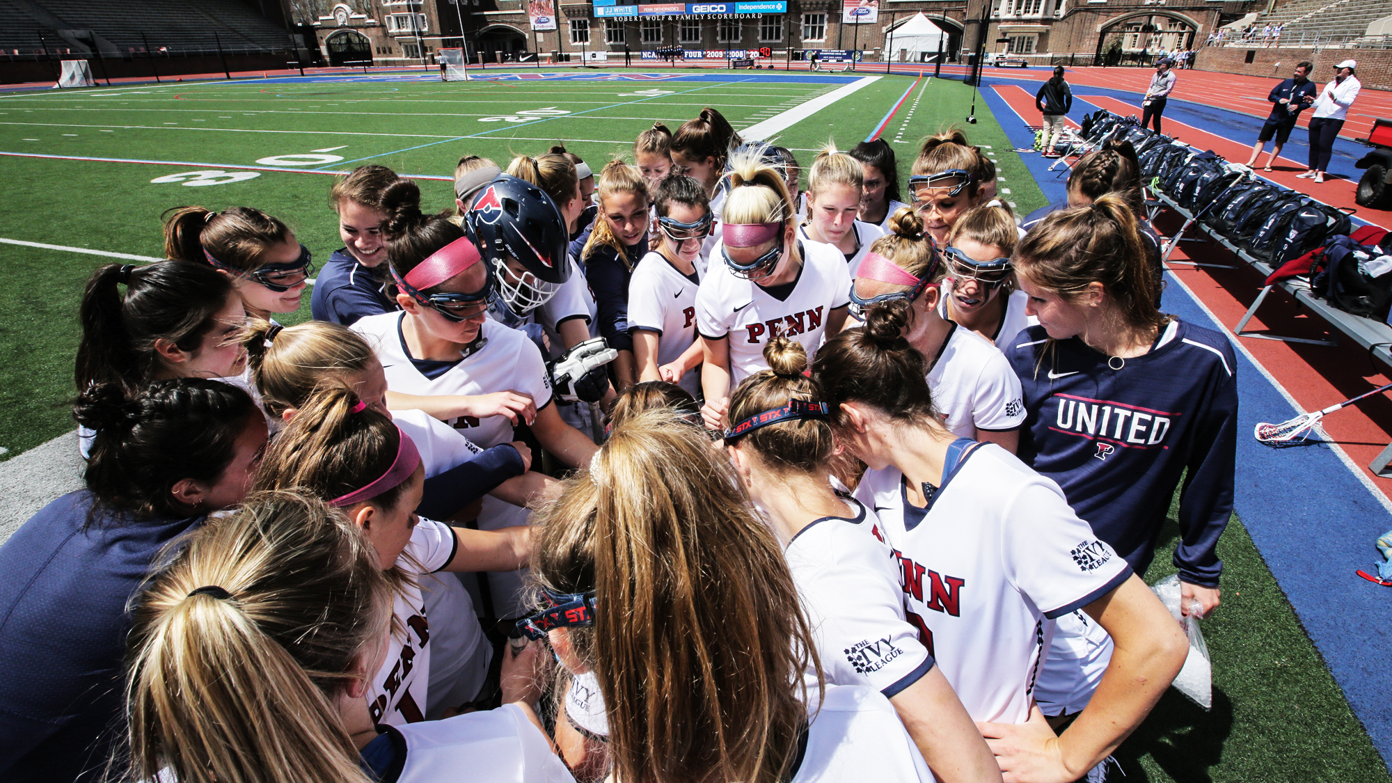 Women's lacrosse players put their hands in a circle on the sideline.
