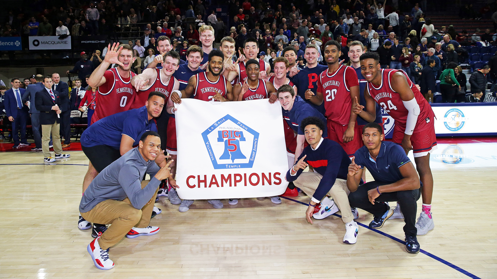 Penn basketball players holder the Big 5 championship banner on the Palestra court