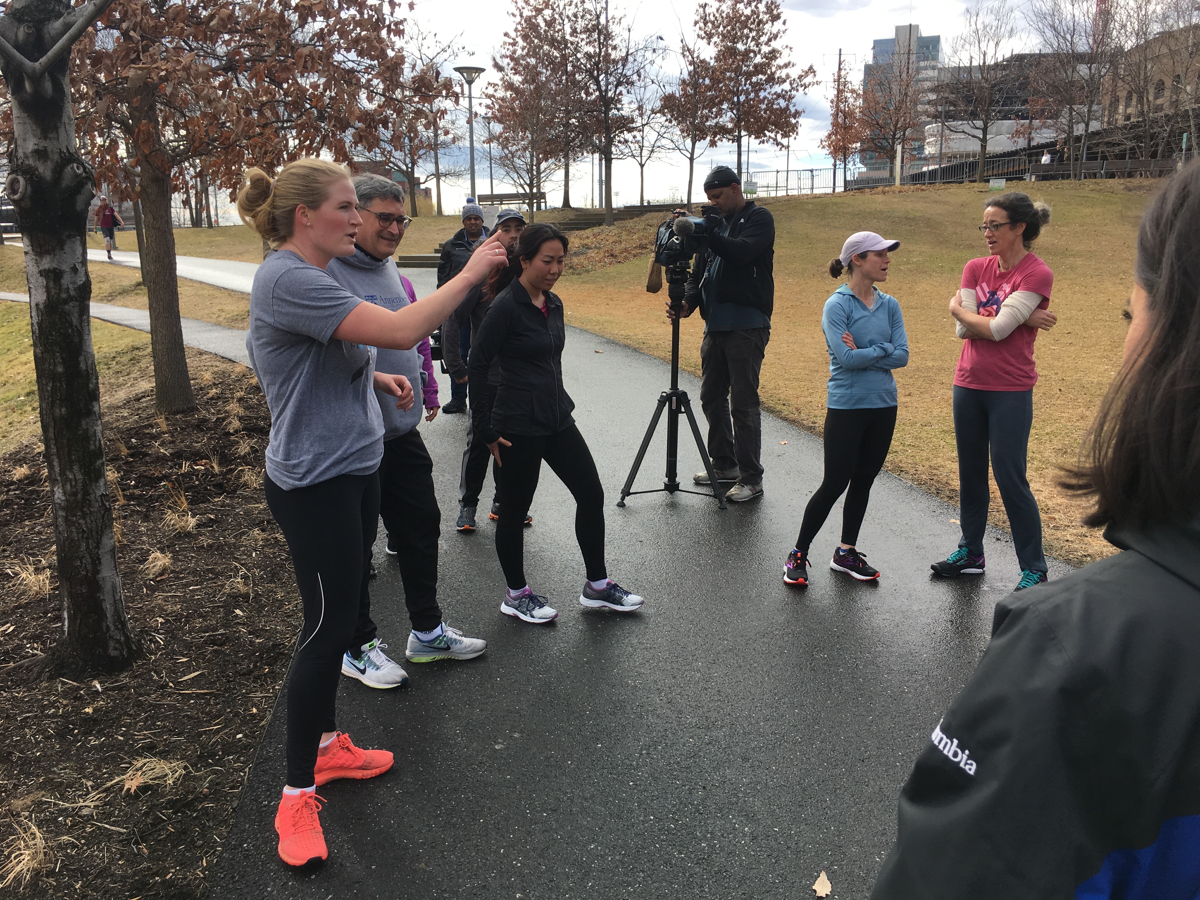 People in exercise clothing standing in a group on a path talk while a videocamera person takes footage.