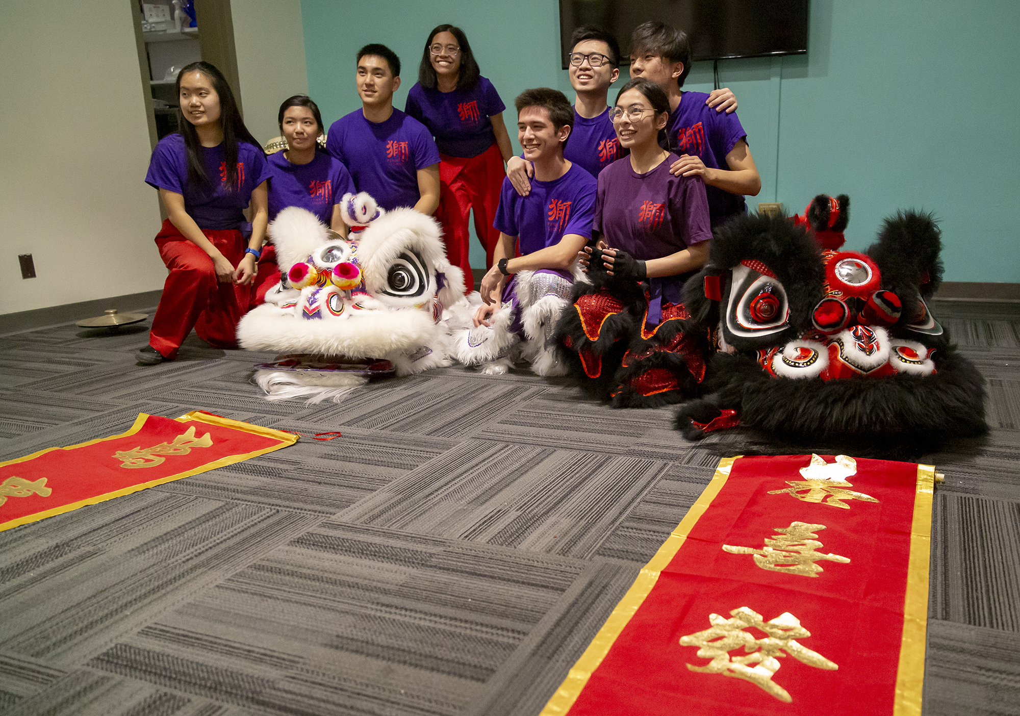 Eight students gathered together with two lion heads and scrolls with Chinese letters. 
